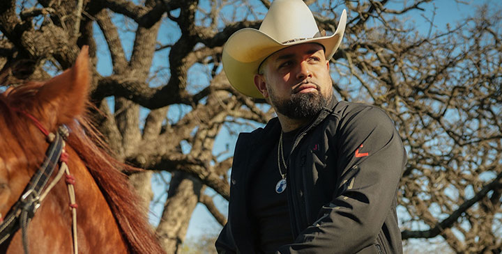 A man, Louie The Singer, dressed as a cowboy, riding a red horse.
